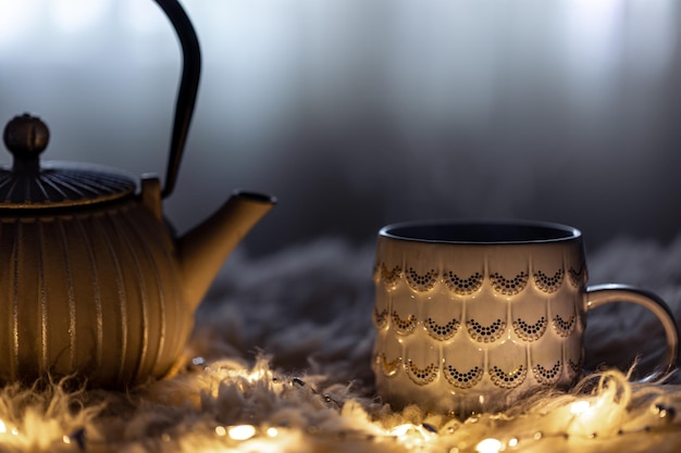 Teapot and cup on a blurred background in the dark with garlands