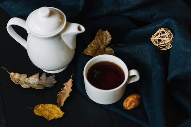 Free photo teapot and cup near leaves and drapery