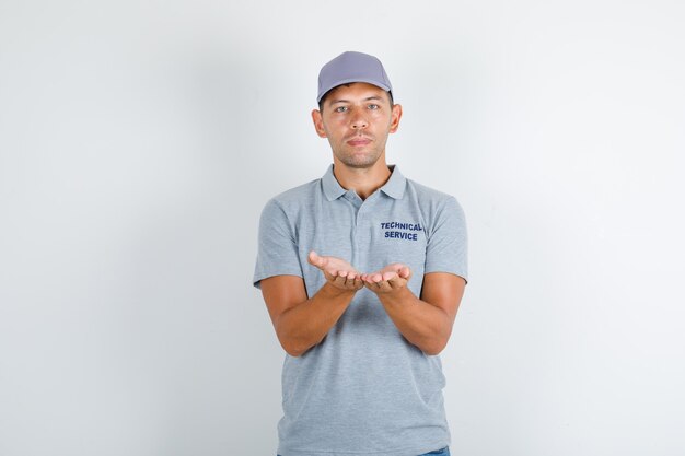 Free photo technical service man keeping opened palms together in grey t-shirt with cap