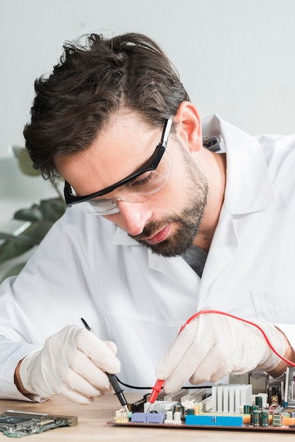 Free photo technician examining computer motherboard with digital multimeter