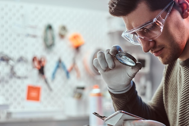 Free photo the technician uses a magnifying glass to carefully inspect the internal parts of the smartphone in a modern repair shop