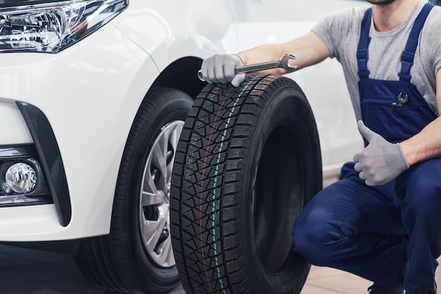 Free photo technician with a blue workwear, holding a wrench and a tire while showing thumb up