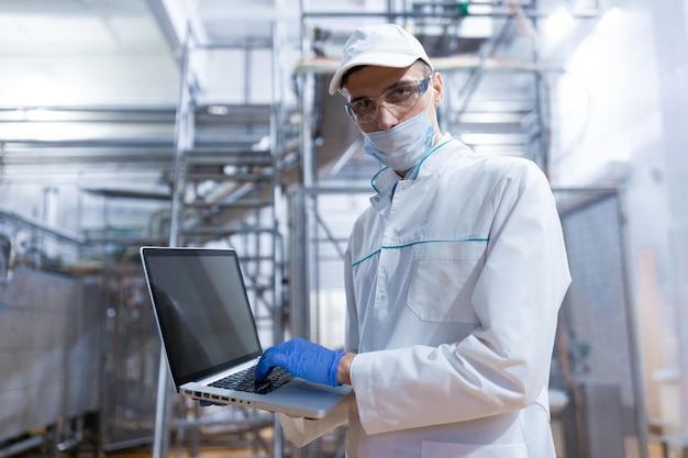 Free photo technologist in a white coat with a laptop in his hands controls the production process in the dairy shop place for writing technologist with a laptop computer is at the factory