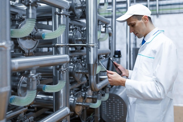 Free Photo technologist with grey tablet in his hands make a set up of the production line while standing at the department of dairy factory