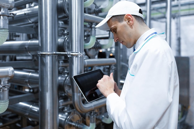 Free Photo technologist with grey tablet in his hands make a set up of the production line while standing at the department of dairy factory