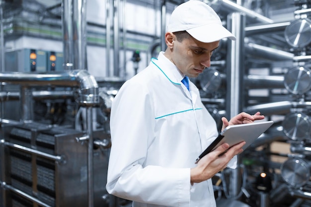 Free Photo technologist with grey tablet in his hands make a set up of the production line while standing at the department of dairy factory