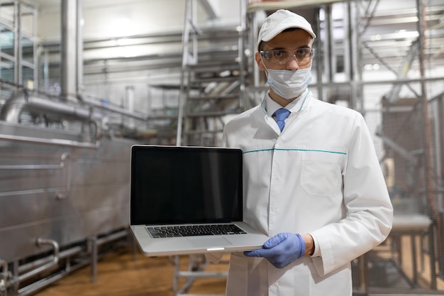 Technologist with laptop in his hands make a set up of the production line while standing at the department of dairy factory