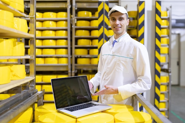 Technologist with laptop in his hands make a set up of the production line while standing at the department of dairy factory