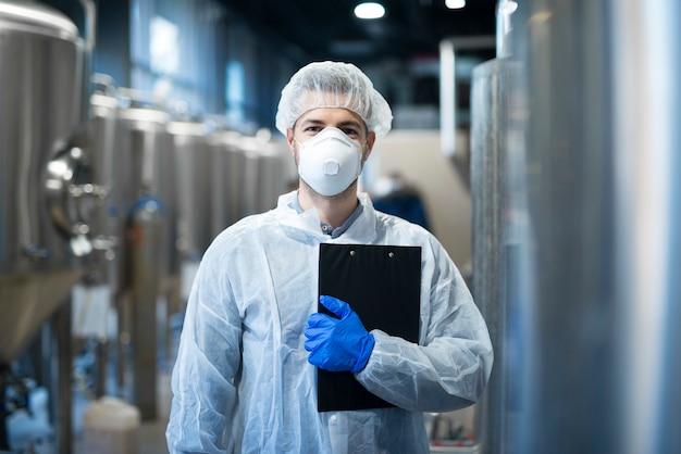 Technologist with protective mask and hairnet standing at factory production line