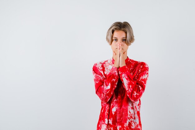 Teen blonde male in oversized shirt with hand in praying gesture and looking focused , front view.