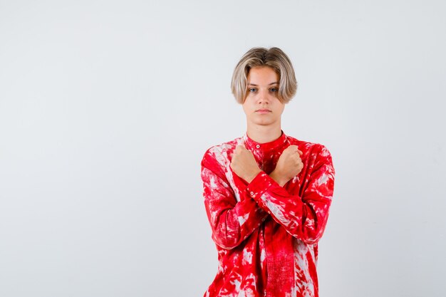 Teen blonde male showing protest gesture in oversize shirt and looking cheerless. front view.