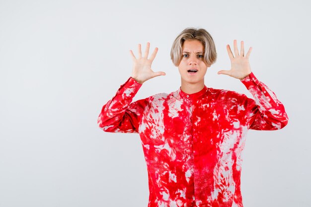 Teen blonde male showing surrender gesture in oversize shirt and looking bewildered. front view.