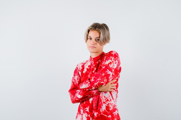 Teen blonde male with arms folded while posing in oversized shirt and looking pensive. front view.