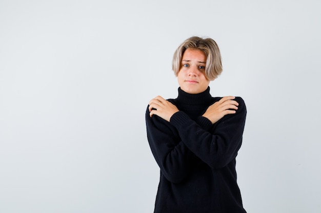 Teen boy in black sweater holding herself and looking upset , front view.