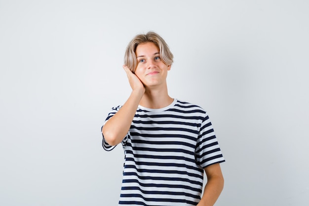 Teen boy keeping hand on head in t-shirt and looking cheerful , front view.