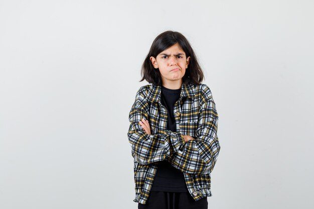 Teen girl in casual shirt holding arms folded, curving lower lip and looking grumpy , front view.