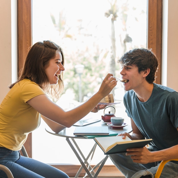 Teen girl feeding boyfriend with dessert in library