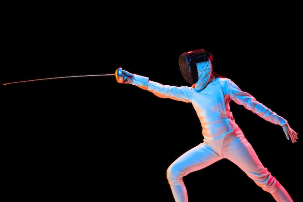 Free photo teen girl in fencing costume with sword in hand isolated on black background, neon light.