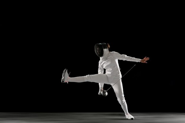 Teen girl in fencing costume with sword in hand isolated on black