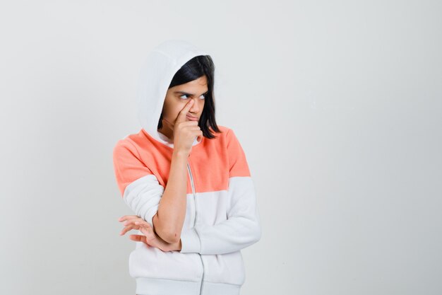 Teen girl holding finger on her cheek in sweatshirt and looking lost.