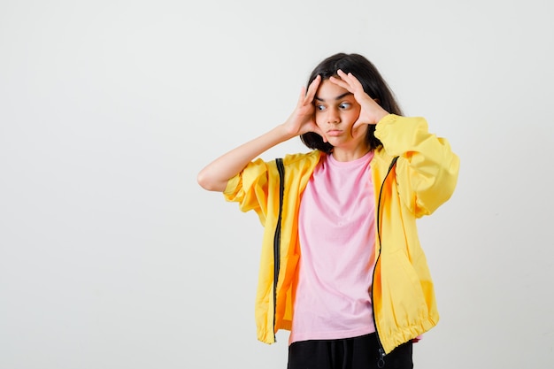 Teen girl keeping hands on face in t-shirt, jacket and looking pensive , front view.