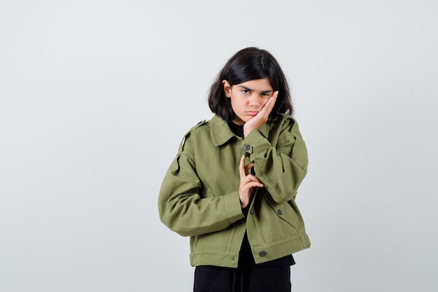 Teen girl leaning cheek on the palm in green jacket and looking tired , front view.