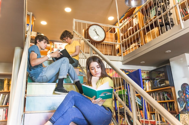 Teen girl reading book on steps near classmates