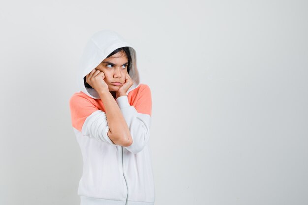 Teen girl in sweatshirt clasping face with fists and looking offended.