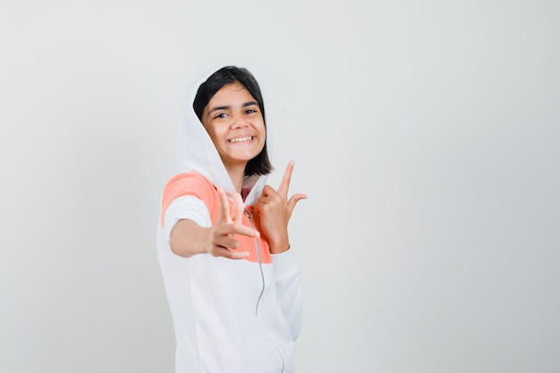 Teen girl in sweatshirt pointing at front while pointing up and looking cheerful.