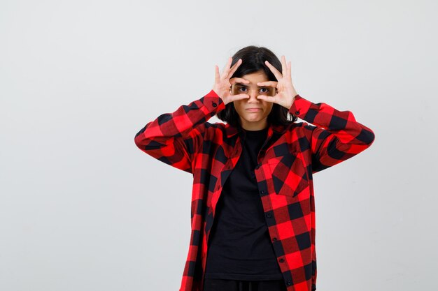 Teen girl in t-shirt, checkered shirt looking through fingers and looking confident , front view.