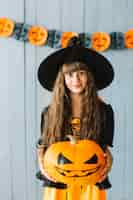 Free photo teen girl in witch costume holding pumpkin