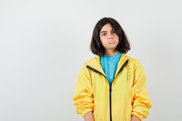 Teen girl in yellow jacket curving lower lip and looking clueless , front view.