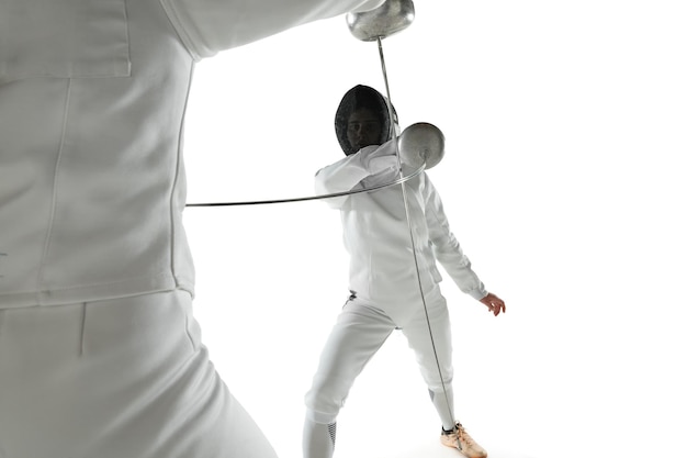 Free photo teen girls in fencing costumes with swords in hands isolated on white studio background. young female models practicing and training in motion, action. copyspace.