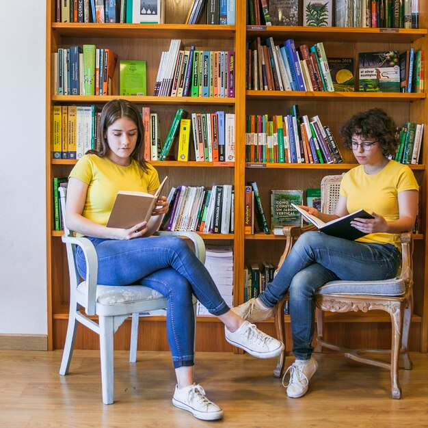 Free Photo teen girls reading on chairs near bookcase