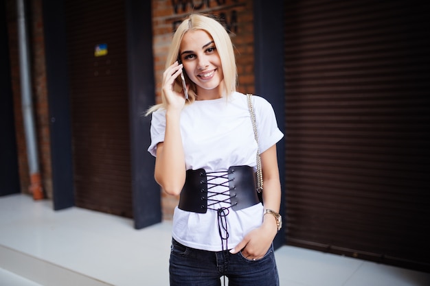 Free Photo teen using cell phone. young blond woman talk at a smartphone while walking on a city street.