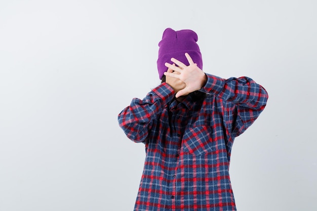 Free photo teen woman in checkered shirt and beanie gesticulating isolated