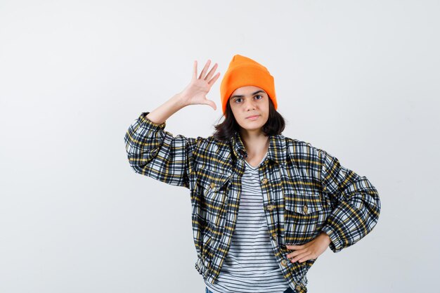 Teen woman in checkered shirt and beanie gesticulating isolated