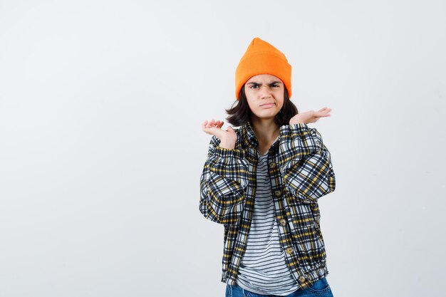 Teen woman in checkered shirt and beanie gesticulating isolated