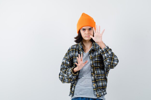 Teen woman in checkered shirt and beanie gesticulating isolated