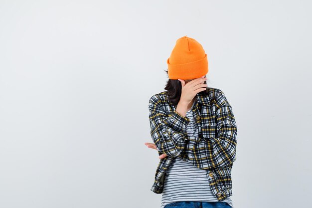 Teen woman in checkered shirt and beanie gesticulating isolated