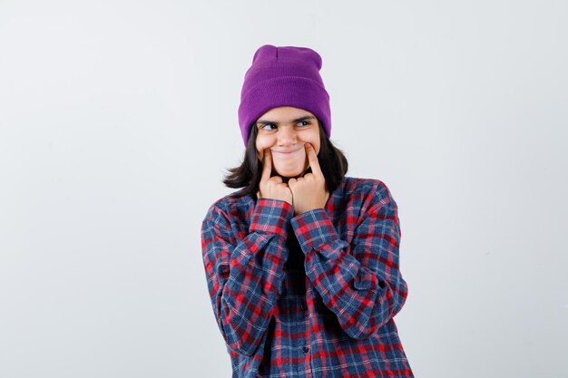 Teen woman in checkered shirt and beanie gesticulating isolated