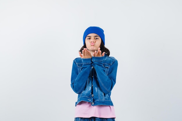 Free Photo teen woman in pink t-shirt jean jacket and beanie blowing air kisses