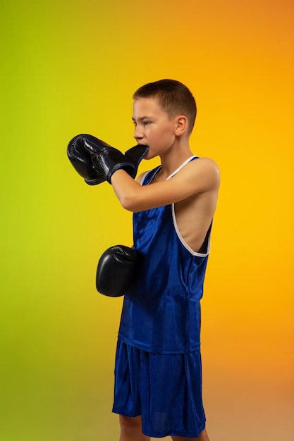 Teenage boxer against gradient neon studio in motion of kicking, boxing