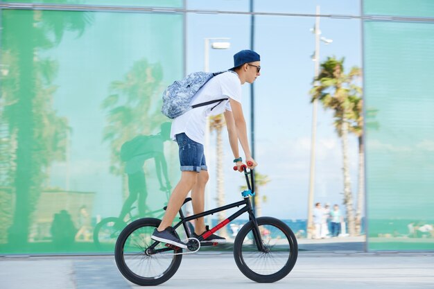 Teenage boy with backpack and wearing cap on bicycle