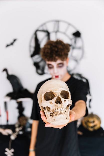 Free photo teenage boy with halloween zombie grim holding skull