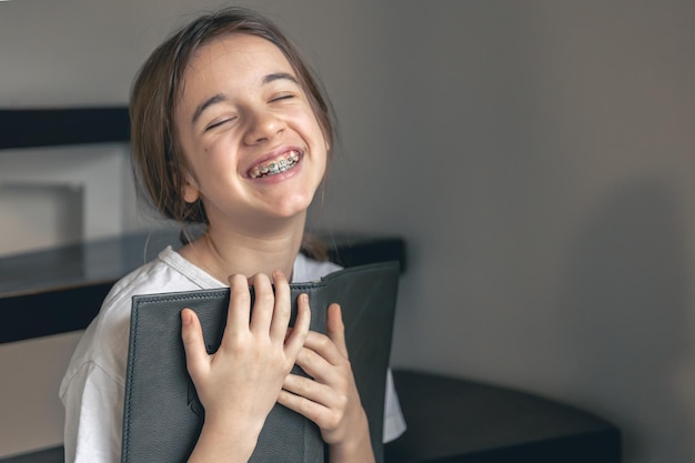 A teenage girl reads a book and smiles showing her teeth with braces