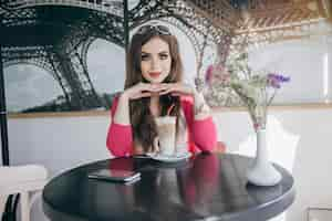 Free photo teenage girl sitting at a glass table with a chocolate smoothie