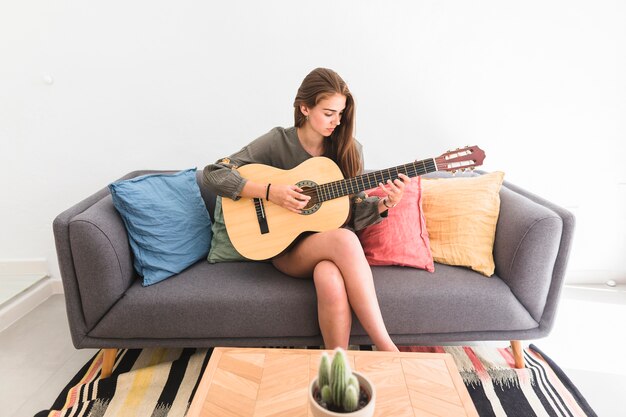 Teenage girl sitting on sofa playing guitar