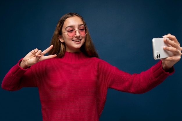 Free Photo teenage girl taking a selfie of herself while showing the peace sign