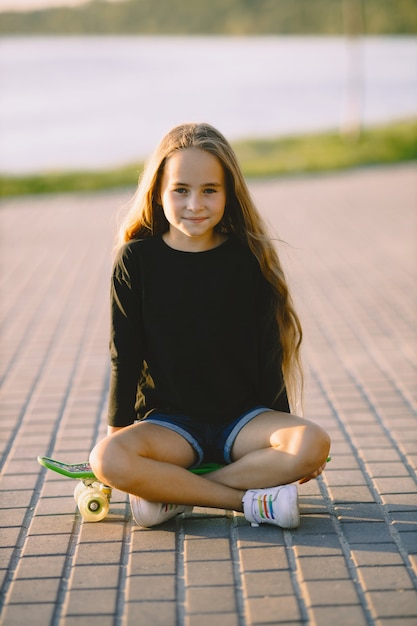 Teenage girl with skateboard sitting by lake